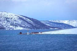 lite fyr utterst på et nes. Vinterlandskap med skogdekte åser