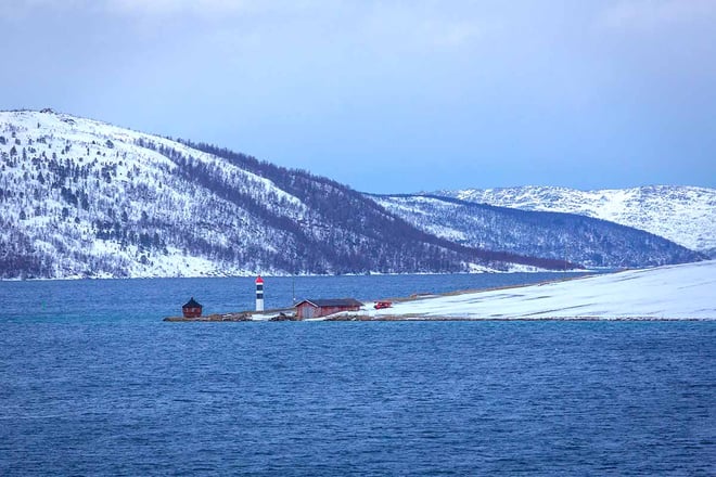 lite fyr utterst på et nes. Vinterlandskap med skogdekte åser