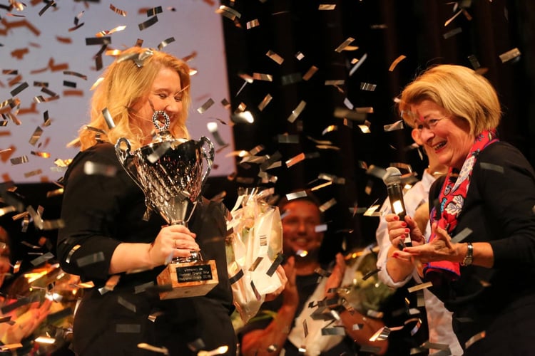 Dame mottar pokal for seier i Forsker Grand Prix mens gullkonfetti daler ned fra taket.