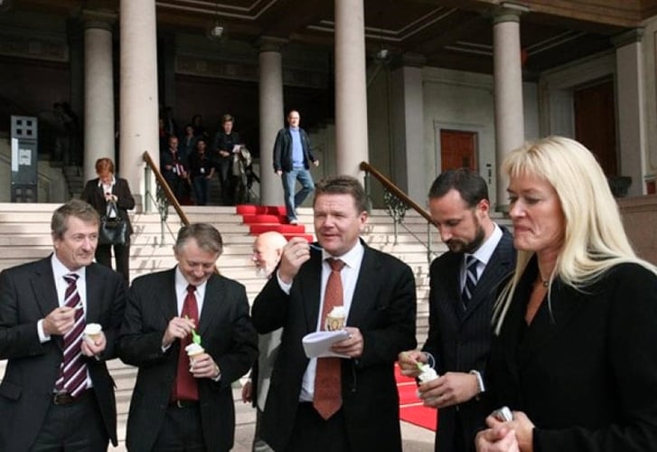 Flere dresskledde menn og en dame spiser softis sammen med H.K.H Kronprins Haakon foran en rød løper. 