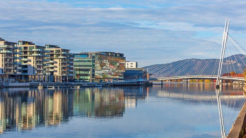 Moderne blokkbebyggelse speiles i elv. Over elven går det en skråkabelbrp som ser ut som en Y ovenfra
