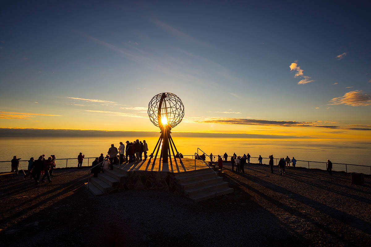En åpen kule med spiler som illustrerer lenge- og breddegrader. Mennesker ved siden av. Solnedgang