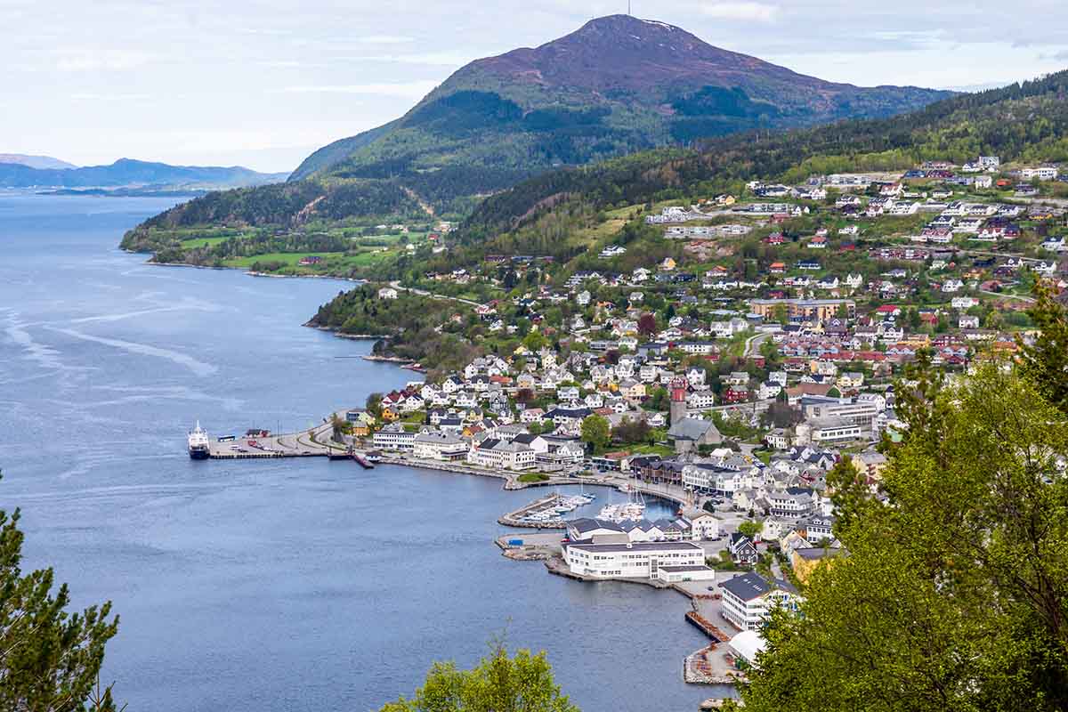 Oversiktsbilde over en liten by som ligger langs kysten. Fjell i bakgrunnen