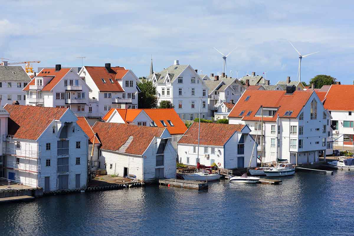 To rader med hvite kysthus langs elvebredden. Vindmøller i bakgrunnen