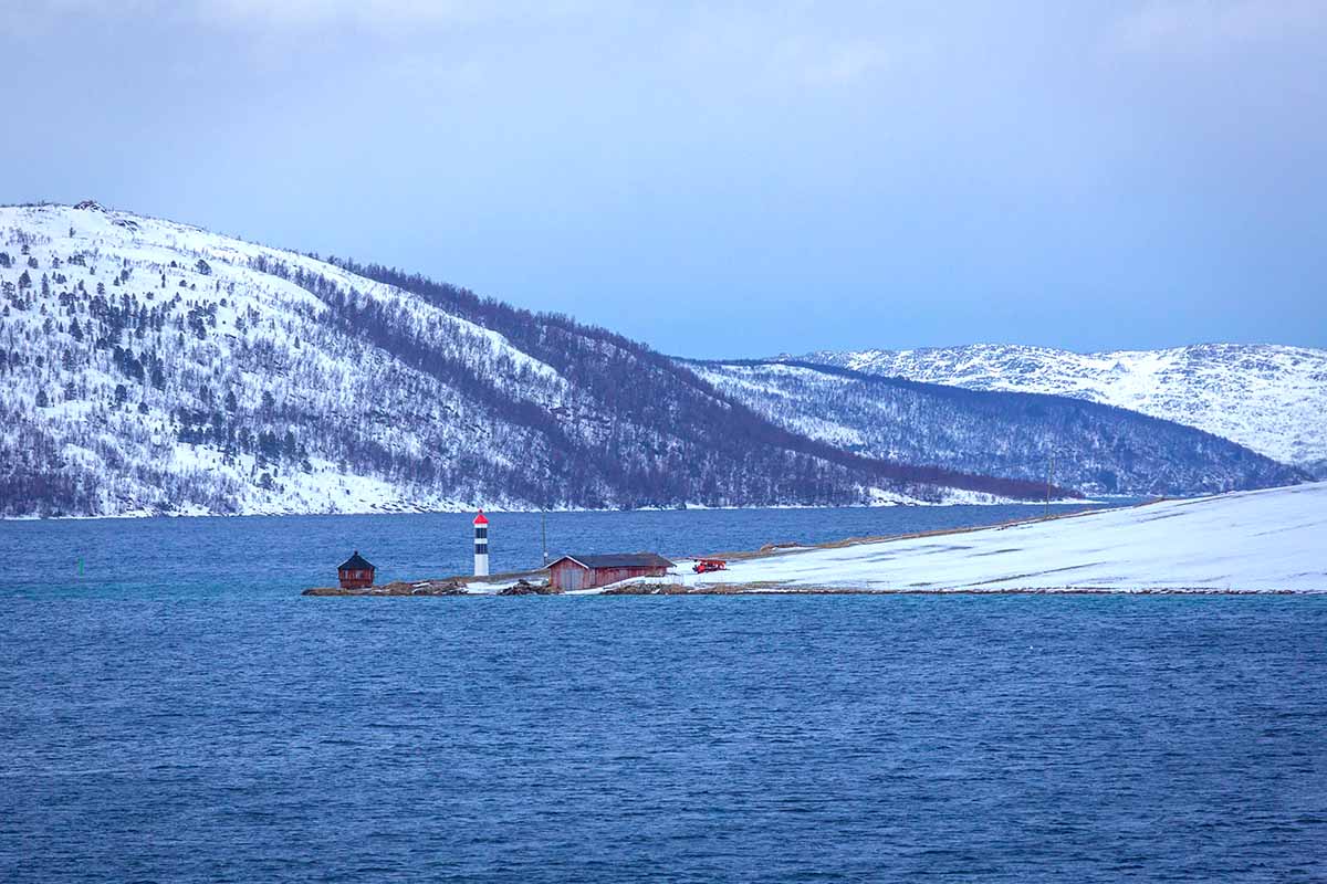 lite fyr utterst på et nes. Vinterlandskap med skogdekte åser