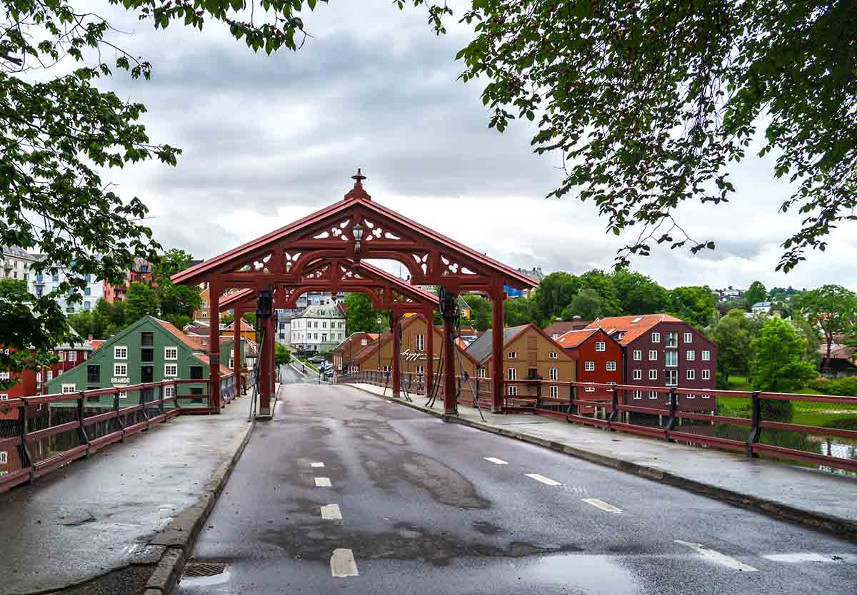 Rød trebro med overbygning. Utsikt mot trehusområde i rødt, oker og grønt