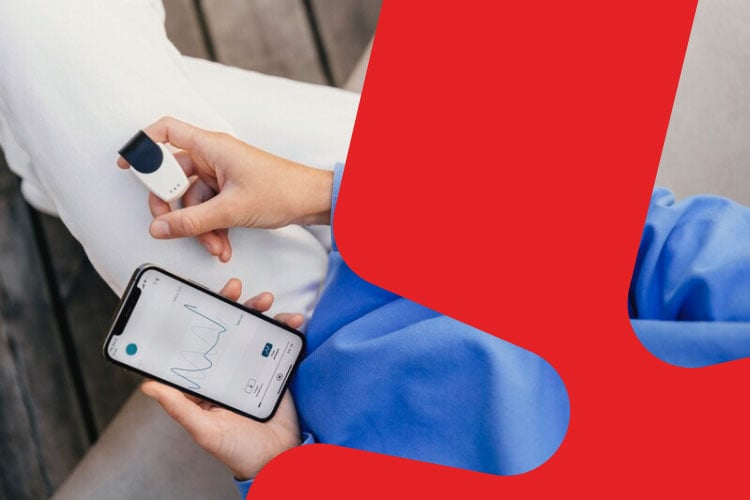 Utsnitt av sittende kropp med hvit bukse og genser. Forsker holder en mobil og måleapparat i hendene.